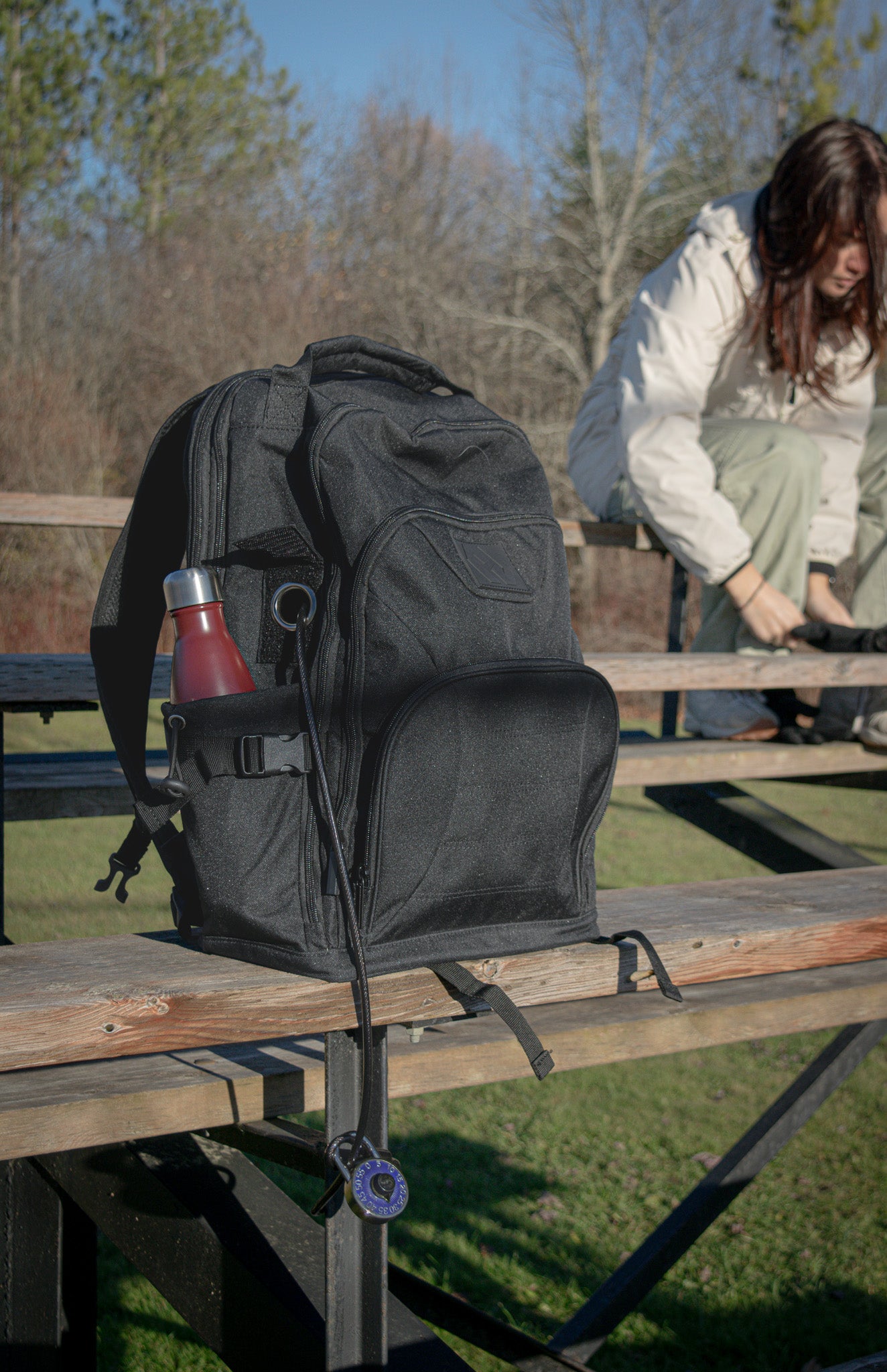 The Havlar backpack locked to baseball stands. A woman in the background ties her shoe.